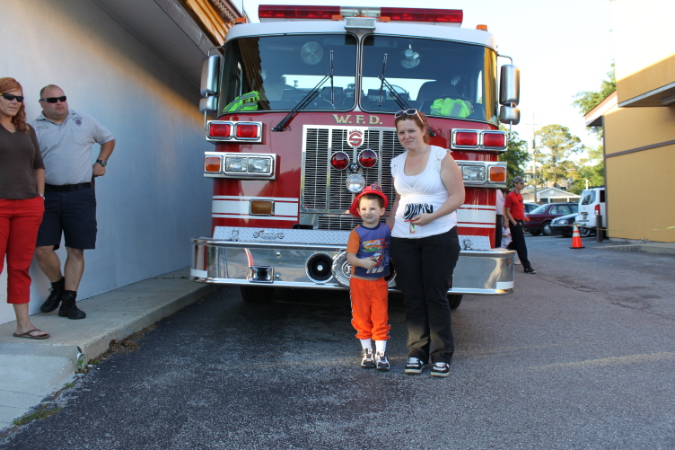 A woman and a young child stand in front of a large red fire engine