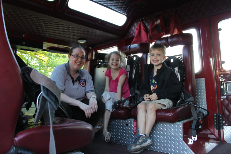 A woman and two children inside the cab of a red fire truck