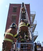 Firefighters in full turnout gear climbing an extended ladder